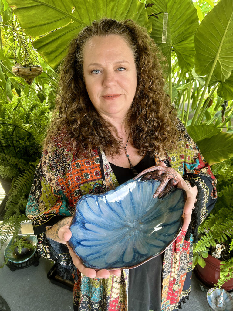 Southern California porcelain artist Leona Darnell of Effie Barks Porcelain Works is holding a handmade sculpted porcelain bowl. The bowl features organic, root-like forms and a textured, earthy exterior that contrasts with a smooth, flowing interior glaze. 